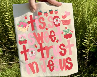 May include: A light beige tea towel with the text "Tis so sweet to trust in Jesus" in pink and red lettering. The towel is decorated with strawberries, a cupcake, and cherries.