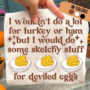 May include: Off-white t-shirt with the text "I wouldn't do a lot for turkey or ham but I would do some sketchy stuff for deviled eggs." The design includes three deviled egg illustrations in brown text.