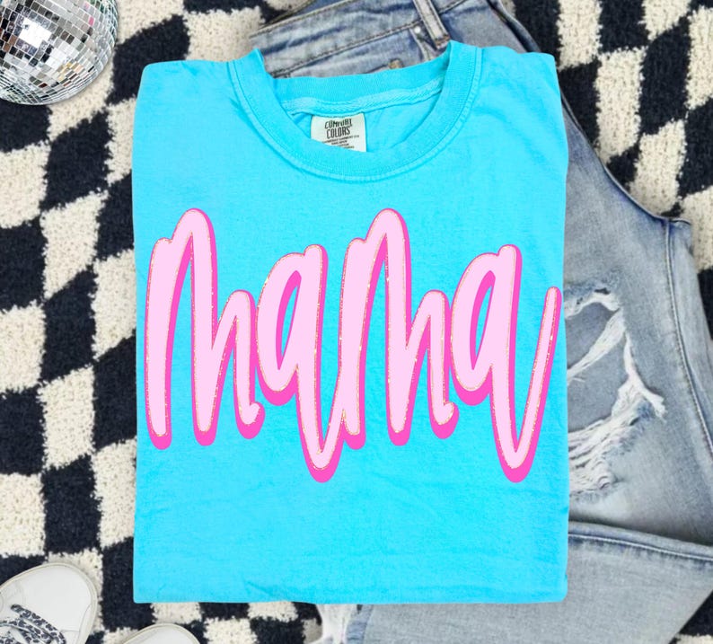 Op de afbeelding: Een fel turquoise t-shirt met korte mouwen waarop het woord mama is gedrukt in een gestileerd roze lettertype met een lichtroze omlijning. Het shirt heeft een ronde hals en een Comfort Colors merklabel zichtbaar bij de kraag.