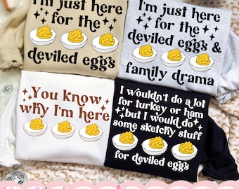 May include: Four sweatshirts in beige, light gray, white, and black, each featuring graphic prints of deviled eggs and text. The text includes phrases like I'm just here for the deviled eggs, family drama, and I would do some sketchy stuff.