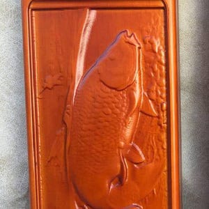 May include: A wooden box with a carved fish design. The box is a rich orange colour and has metal clasps.