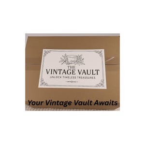 May include: A cardboard box with a white label that reads "THE VINTAGE VAULT" with the tagline "UNLOCK TIMELESS TREASURES." Below the label is the text "Your Vintage Vault Awaits."