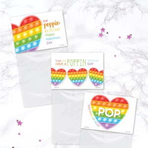 May include: Valentine's Day cards with heart-shaped pop-it toys in rainbow colors. The cards have text that says "Just poppin by to say Happy Valentine's Day", "Hope you have a poppin Valentine's Day", and "You make my heart POP".