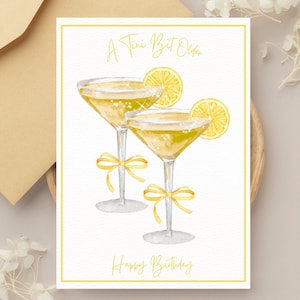 May include: A birthday greeting card with two watercolor martini glasses, each garnished with a lemon slice and a yellow bow. The card has the text "A Tiny Bit Older" and "Happy Birthday" in elegant script.