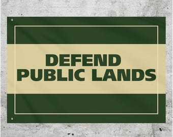 May include: A green and beige rectangular sign with the text "DEFEND PUBLIC LANDS" in black.
