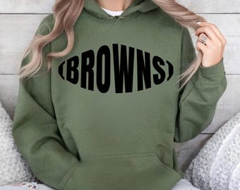 May include: An olive green hoodie with a black oval-shaped text that reads "BROWNS". The hoodie has a front pocket and a hood. The design is simple and bold, perfect for fans of the Cleveland Browns.