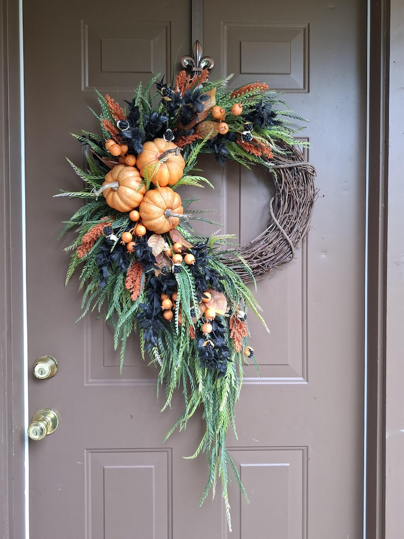 This elegant cascading pumpkin Halloween wreath is handcrafted using high quality artificial orange pumpkins, cascading sawgrass greenery, beaded leaf ferns, black leaves, orange foxtails, and orange berries crafted on a natural grapevine base.