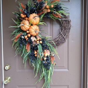 This elegant cascading pumpkin Halloween wreath is handcrafted using high quality artificial orange pumpkins, cascading sawgrass greenery, beaded leaf ferns, black leaves, orange foxtails, and orange berries crafted on a natural grapevine base.
