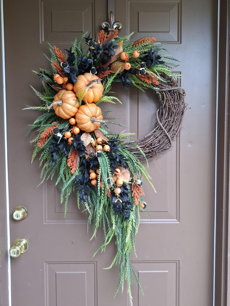 This elegant cascading pumpkin Halloween wreath is handcrafted using high quality artificial orange pumpkins, cascading sawgrass greenery, beaded leaf ferns, black leaves, orange foxtails, and orange berries crafted on a natural grapevine base.