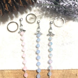 May include: Three angel keychains with a silver angel charm and a beaded chain. The chains are pink, light blue, and dark blue.