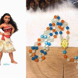 May include: A rosary with blue, orange, and white beads. The rosary features a gold-colored centerpiece with a religious figure and a cross at the end. The beads are strung on a gold-colored chain.