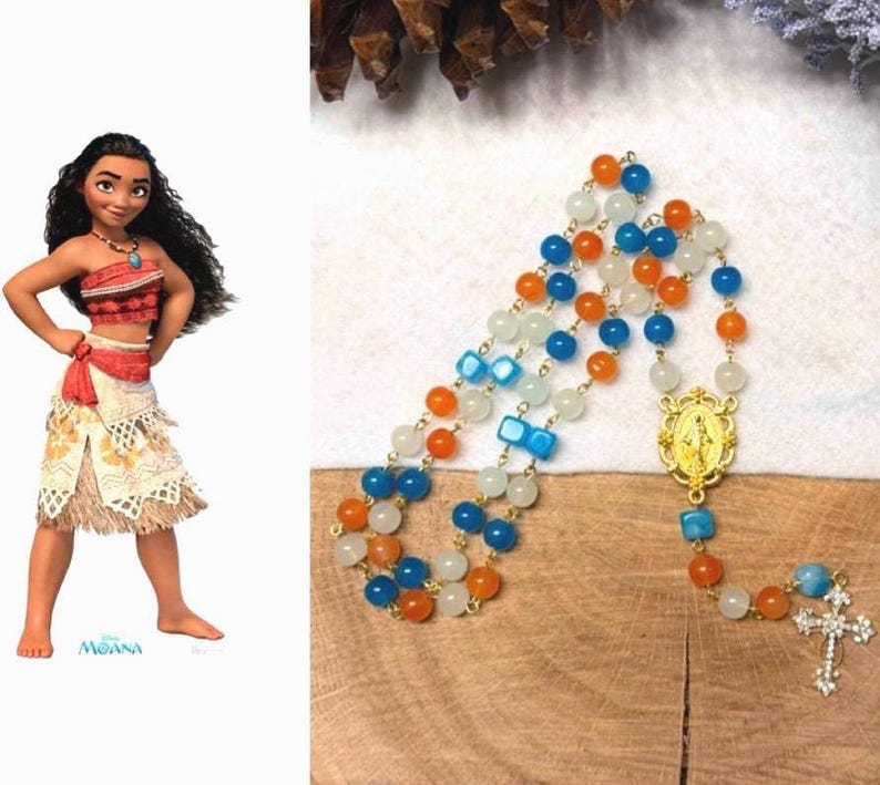 May include: A rosary with blue, orange, and white beads. The rosary features a gold-colored centerpiece with a religious figure and a cross at the end. The beads are strung on a gold-colored chain.