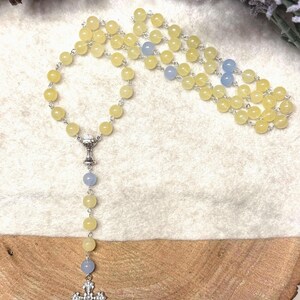 May include: A rosary with yellow and blue beads. The beads are strung on a silver chain. The rosary has a silver cross pendant at the bottom and a silver chalice-shaped connector.