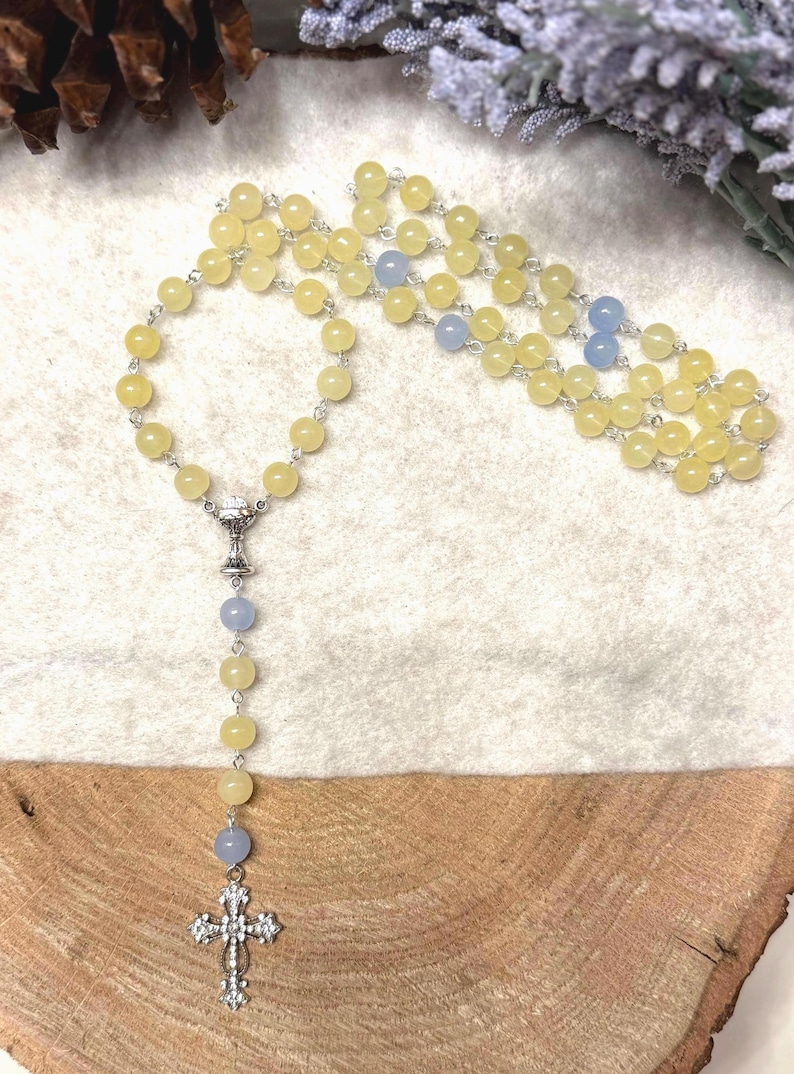 May include: A rosary with yellow and blue beads. The beads are strung on a silver chain. The rosary has a silver cross pendant at the bottom and a silver chalice-shaped connector.