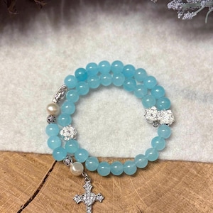 May include: A double-strand bracelet made of light blue beads with a silver cross charm and white pearl accents.