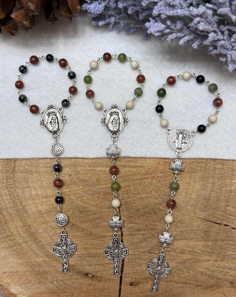 Puede incluir: Tres pulseras de rosario con eslabones de metal plateado, medallones religiosos circulares con figuras y peque&ntilde;os dijes de cruz. Las pulseras est&aacute;n compuestas por cuentas redondas en colores negro, marr&oacute;n, verde y crema.