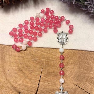 May include: A rosary with pink and white beads. The beads are strung on a silver chain. The rosary features a silver cross and a silver pendant with an image of the Virgin Mary.