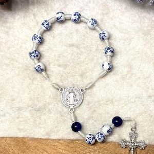 Op de afbeelding: Witte en blauwe bloemmotief rozenkrans kralen met een zilveren St. Christopher-medaille en een zilveren kruis met strass.