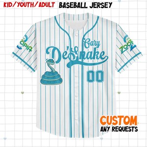 Puede incluir: Camiseta de b&eacute;isbol blanca con rayas azules verticales. Presenta el texto "De'Snake" en escritura turquesa, un gr&aacute;fico de serpiente turquesa y el n&uacute;mero "00". Las mangas tienen los logotipos "ZOOT" y "OPIA". El texto "CUSTOM ANY REQUESTS" est&aacute; en la parte inferior.