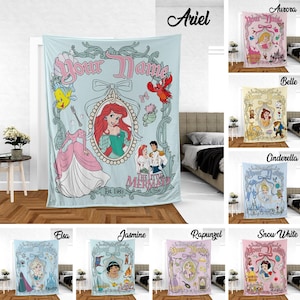 May include: A light blue blanket featuring Ariel from The Little Mermaid, with the text "Your Name" and "Est. 1989". The design includes illustrations of Ariel, Flounder, Sebastian, and other elements from the movie.