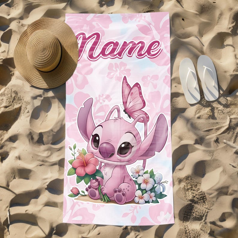 Pode incluir: Toalha de praia rosa com um personagem de desenho animado segurando flores, uma borboleta e a palavra "Name". A toalha tem um padr&atilde;o floral e est&aacute; na areia, ao lado de um chap&eacute;u de palha e chinelos brancos. A toalha tem cerca de 170 cm de comprimento.