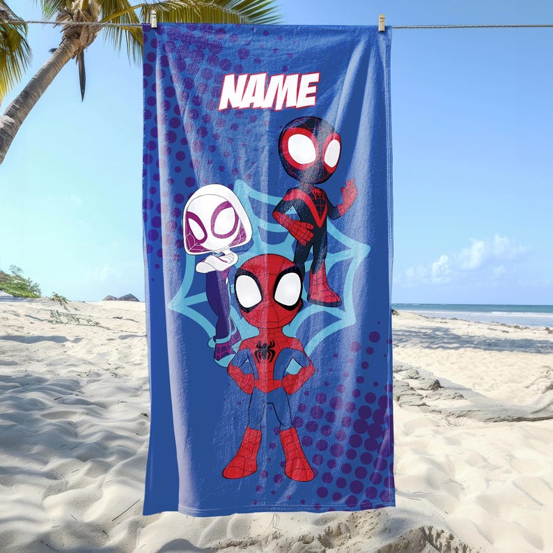 May include: Blue beach towel with cartoon Spider-Man characters. The towel has the word "NAME" in white block letters at the top. The background includes a beach and palm tree.