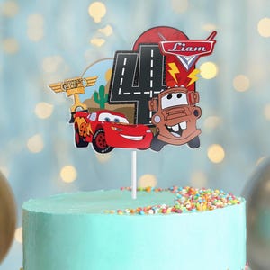 May include: A cake topper featuring Lightning McQueen and Mater from the Cars movie, with a number 4 and the name "Liam". The topper includes a Piston Cup emblem and a road design, all on a blue cake with colorful sprinkles.