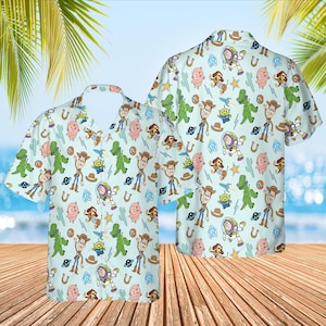 May include: Two light blue short-sleeved shirts with a repeating pattern of Toy Story characters, including Woody, Buzz Lightyear, and Rex. The characters are on a light blue background with green cacti, stars, and spaceships.