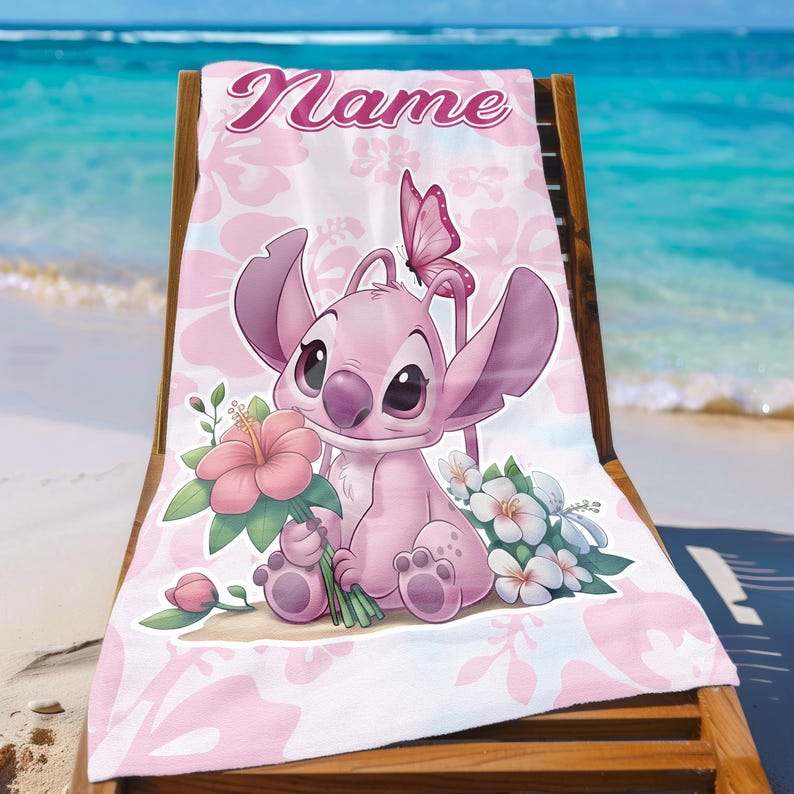 Pode incluir: Toalha de praia rosa com um personagem de desenho animado segurando flores, uma borboleta e a palavra "Name". A toalha, com estampa floral, est&aacute; sobre uma cadeira de praia de madeira, com o mar ao fundo.