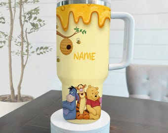 May include: A yellow insulated tumbler featuring a honey-themed design with a dripping honey effect, a beehive, and the word "NAME". The bottom of the tumbler showcases illustrations of Winnie the Pooh, Tigger, and Eeyore.