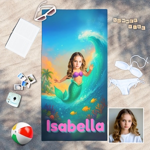 May include: A beach towel featuring a mermaid design with the name "Isabella" in pink. The towel has a vibrant illustration of a girl as a mermaid in front of a large wave. The words "Summer Vibe" are spelled out in wooden blocks.