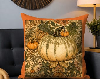 May include: Square orange throw pillow featuring a vintage-style pumpkin illustration. The design includes a large, detailed pumpkin with a smaller one, set against a backdrop of floral and leaf patterns in shades of green, orange, and beige. The pillow is on a gray couch.