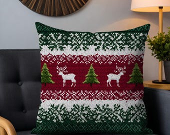 May include: Square cushion with a festive Christmas sweater design. The cushion features a pattern of white snowflakes, reindeer, and green Christmas trees on a red background. The top and bottom borders are green.