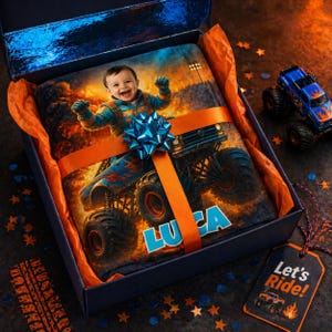 May include: A personalized blanket featuring a child driving a blue monster truck with flames, inside a dark blue gift box with orange tissue paper and a blue bow. The name LUCA is printed in large blue letters. A tag reads Let's Ride!