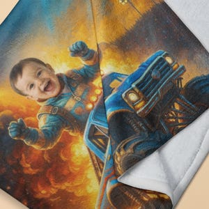 May include: A soft plush blanket featuring a vibrant, colorful print of a smiling child wearing a blue flight suit, positioned next to a large blue monster truck. The background displays a fiery, orange and yellow explosion with dark smoke.