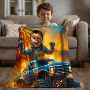 May include: A rectangular throw blanket featuring a vibrant, colorful graphic print of a smiling child wearing a blue jacket, positioned above a blue monster truck with orange flame decals against a bright yellow and orange sunset background.