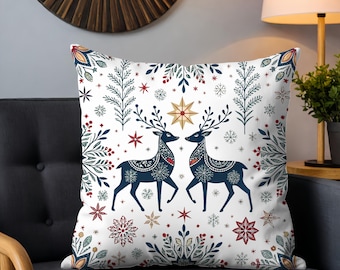 May include: Square decorative pillow with a white background featuring two navy blue reindeer facing each other. The pillow has a festive design with snowflakes, stars, and floral elements in red, green, and gold.