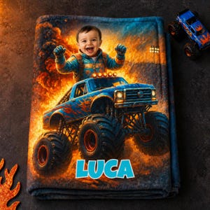 May include: A blue and orange monster truck blanket featuring a smiling child in a blue jacket. The blanket has the name "LUCA" in white block letters. Two toy monster trucks are visible in the background.