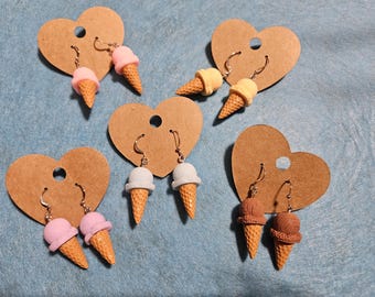 Puede incluir: Cuatro pares de pendientes de cono de helado en tarjetas marrones en forma de corazón. Los pendientes están hechos de arcilla polimérica y están disponibles en rosa, amarillo, azul y marrón.