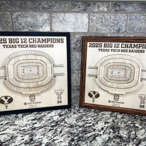 May include: Two wooden plaques with laser-cut stadium designs. The plaques are framed, one in black and one in brown. Text on the plaques reads "2025 BIG 12 CHAMPIONS TEXAS TECH RED RAIDERS" and includes the AT&T Stadium logo.