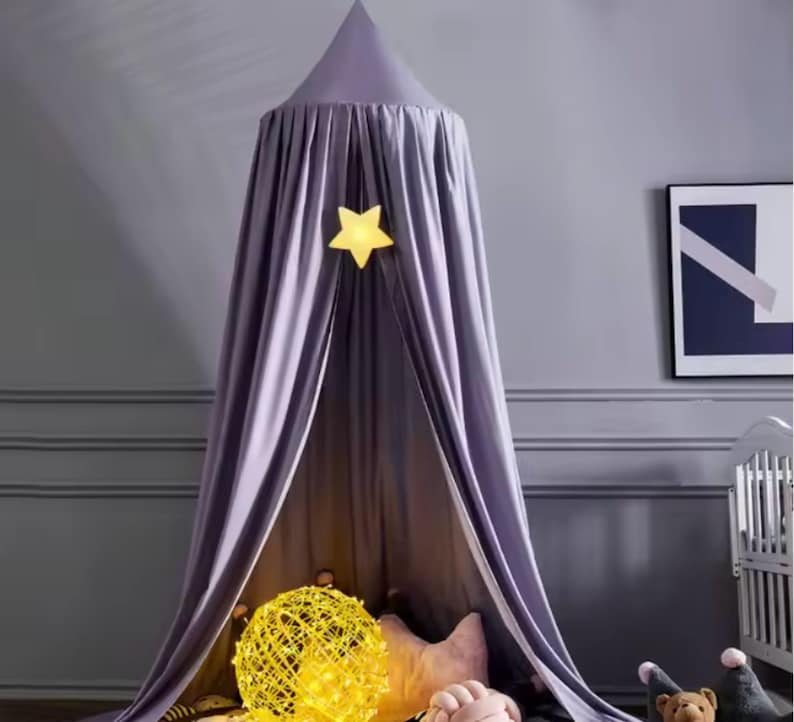 May include: A lavender-colored canopy bed with a star-shaped light fixture. The canopy is draped and hangs from the ceiling, creating a cozy space. A yellow decorative ball and stuffed animals are visible below.