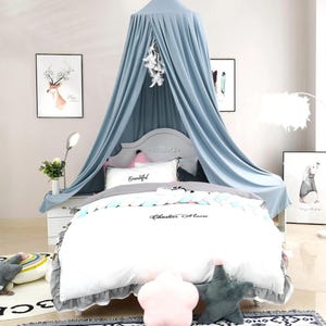 May include: A light blue canopy bed with a white comforter set. The comforter has the text "Cheshire Moore" on it. Decorative pillows and artwork of a deer and a rabbit are also present.