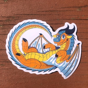 Puede incluir: Una pegatina de un drag&oacute;n de dibujos animados con escamas azules y naranjas. El drag&oacute;n est&aacute; enroscado con las alas extendidas. La pegatina est&aacute; sobre una superficie de madera.