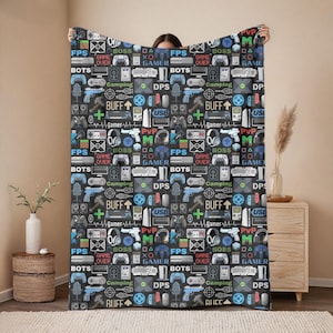 May include: A black and white patterned fleece blanket with a gamer theme. The blanket features various gaming icons, including controllers, headsets, and text like "FPS", "BOSS", "GAME OVER", "GAMER", "BOTS", "CAMPING", "DPS", "BUFF", "USE", and "PVP".