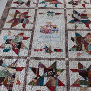 May include: A quilt with a patchwork design featuring a variety of colors and patterns. The quilt is made up of squares with a star design in each square. The center square features an embroidered image of four teddy bears with a verse about love and family.