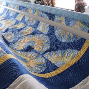 May include: A blue and yellow quilt with a swirling pattern is being quilted on a long arm quilting machine.