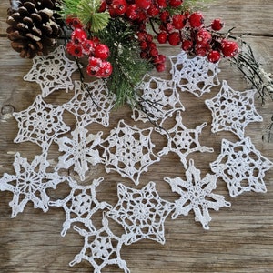 May include: A collection of white crocheted snowflakes on a rustic wooden background. The snowflakes are arranged in a heart shape and are surrounded by red berries and green foliage.