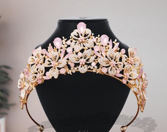 May include: A gold-toned bridal tiara with pink and clear gemstones, displayed on a black mannequin head. The tiara features floral and leaf designs, with the words "bridal jewelry" visible.