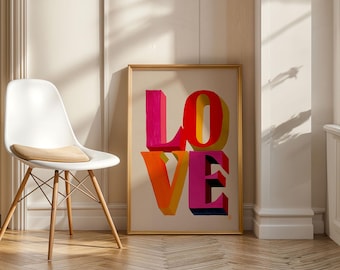 May include: A framed art print with the word "LOVE" in large, colorful 3D letters. The letters are in shades of pink, red, orange, and yellow. A white chair with wooden legs is in the foreground.