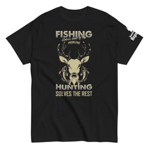 Puede incluir: Camiseta negra con un gráfico de un ciervo con peces en sus astas. El texto "Fishing solves most of my problems" y "Hunting solves the rest" está impreso en la camiseta.
